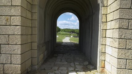 Wall Mural - Stone archway tunnel opening into ancient ruins at Veliki Preslav, Bulgaria. The historic passageway is surrounded by lush green fields and remnants of old stone pathways.