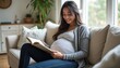 © natakot - A joyful pregnant woman sits comfortably on a soft sofa, engrossed in a book while showcasing her beautiful baby bump. The warm, inviting atmosphere of the room, filled with natural light and greenery