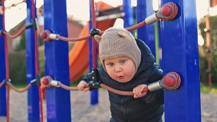 One year old boy in a black jacket runs and plays outside on the playground. Child learns the world. Toddler boy smiles and has fun on the playground.