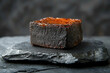 © Vibudhaart - A square piece of cooked meat with a shiny top, placed on a black stone surface.