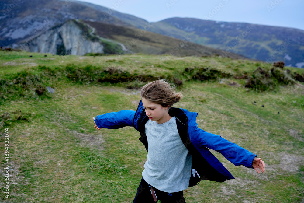 Young boy in blue jacket enjoying outdoors on grassy hillside with