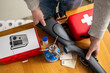 © Connect Images - Person organizing survival gear on a wooden table with a radio and first aid kit. Preparing a survival weekend
