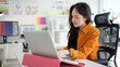 © wattana - Young female designer concentrating on her project at a modern workspace with a laptop and color palettes.