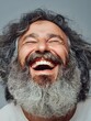 © CHAIYAPHON - A joyful mature man with a long gray beard laughs heartily with eyes closed against a gray background.