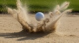 A white golf ball exploding out of a sand trap with sand flying in the air on a sunny day at the golf course