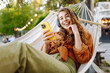 © maxbelchenko - Beautiful woman relaxing in hammock by the lake wearing wireless headphones and using phone. Young woman enjoying sunny weather in park. Concept of relaxation, fun, blogging.