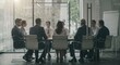 © all is well - A group of business professionals are seated around a conference table in a bright modern office space setting