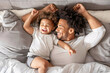 © Alvaro - African American father and son lying on bed, smiling under soft natural light