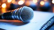 © Art Genie - Close-up of a microphone positioned beside an open notebook on a wooden surface, with a soft focus background showcasing warm bokeh lights for a creative and inspirational atmosphere