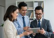 © Aklima - Three business colleagues looking at a tablet screen together in an office setting indoors