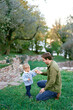 © VolodymyrNadtochii - Dad hands a fruit to a little girl sitting on his knees in front of her on a green lawn
