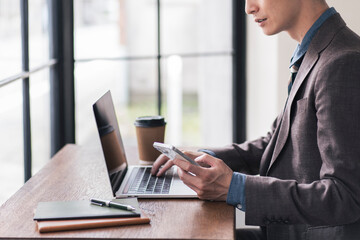 カフェでノートパソコンを開き、スマートフォンを見ながら作業をしている日本人男性。