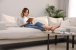© New Africa - Young woman reading book on sofa at home