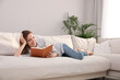 © New Africa - Young woman reading book on sofa at home