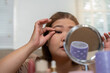 © Natee Meepian - Makeup and Elegance. A woman applying false eyelashes in her beauty routine.