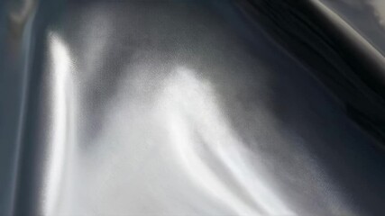 Wall Mural - close-up video of smooth, flowing metallic fabric with a reflective sheen, captured from a low angle