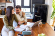 © we.bond.creations - Young smiling couple working from home, using laptop and taking notes while sitting at kitchen table