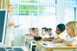 © JackF - Focused preteen pupils studying in classroom with female teacher, writing exercises in workbooks