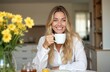 © miss irine - Young blonde woman smiles while drinking tea from white mug. Morning routine at home, enjoying herbal beverage. Cozy living room interior with yellow flowers. Happiness, relaxation, home comfort.