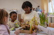 © lordn - Teacher and curious children explore soil and plants in a classroom science activity, encouraging hands-on learning and environmental awareness in a diverse group of students.