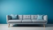 © Shousei - 淡いブルーのマット背景に、ふわっとしたクッションが特徴的な柔らかなグレーのソファが1つ置かれ、落ち着いた温かみのある空間が広がる