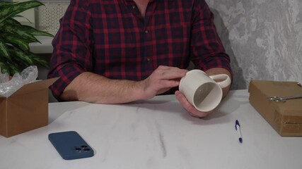Wall Mural - the man takes the packaged mug out of the box, examines it and discovers a defect. damaged order
