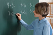 © Pixel-Shot - Cute boy writing on chalkboard during lesson in classroom