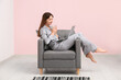 © Pixel-Shot - Young woman in pajamas working with laptop and holding cup of coffee on black armchair at home. Remote work concept
