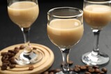 Coffee cream liqueur in glasses and beans on black table, closeup
