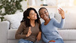 © Prostock-studio - Cute black girlfriends sitting on floor by couch in living room and taking selfie together, using mobile phone, copy space. Happy african american women enjoying weekend at home