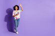 © deagreez - Cheerful young woman in a vibrant printed shirt waving while holding a smartphone against a vibrant purple background
