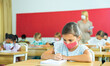 © JackF - Portrait of diligent schoolgirl wearing protective face mask sitting in class writing exercise, new normal education during pandemic