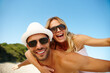 © peopleimages.com - Couple, sunglasses and piggyback on vacation, smile and peace at beach or game by blue sky. People, happy and tropical island for bonding on weekend, outdoor nature and love for marriage or romance