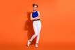 © deagreez - Happy young woman in a stylish outfit posing playfully against a bright orange background, showcasing trendy fashion