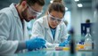 © natakot - A man and a woman, both wearing lab coats and protective goggles, are deeply engaged in scientific research at a sleek laboratory table. Their concentration highlights the dedication and teamwork