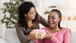 © Prostock-studio - Happy birthday bestie. Black woman giving gift to her happy girlfriend at home