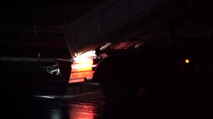Fototapete - Truck spreading gravel on fresh coat of hot liquid bitumen at night, preparing for final asphalt layer – close-up shot

