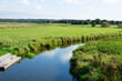 © Olga - River and green meadow. Sky and clouds reflected in water. Wooden stairs leading down to river. Forest in background. Pasture. Countryside. Summer sunny day. Nature. Beauty.