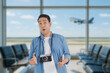 © Mallika - Happy Asian man holding passports and boarding passes at the airport terminal, excited and ready for the trip. Travel and vacation concept with background of airplane taking off.