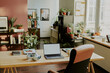 © AnnaStills - High angle shot of cozy it office equipped with work table covered with copybooks and digital devices, spacious room decorated with green plants in pots