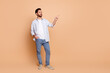 © deagreez - Stylish young man in casual attire pointing to the side against a beige background, creating a confident and promotional mood