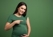 © PP Creative - A smiling pregnant woman in a green shirt pointing to a vaccination bandage on her arm
