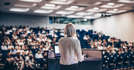Wall Mural - female speaker giving a talk on corporate business conference. unrecognizable people in audience at 