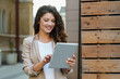 © Dorde - Attractive Businesswoman In Beige Blazer Working On Digital Tablet Outside Modern Building With Wooden Details