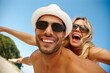 © peopleimages.com - Couple, sunglasses and flying on vacation, smile and peace at beach or game by blue sky. People, piggyback and tropical island for bonding on weekend, outdoor nature and love for marriage or romance