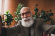 © deagreez - Smiling mature man with white beard posing in elegant suit and retro home interior, surrounded by green plants, expressing happiness