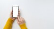 © Sri - A person is holding a cell phone and pointing at the screen. The phone is white and the person is wearing a yellow sweater. Concept of technology and modernity, as well as a casual, everyday moment.
