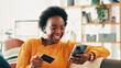© peopleimages.com - Home, credit card and black woman on sofa, smartphone and online payment with smile. Apartment, mobile user and African person on couch, cellphone and banking for transactions, ecommerce and savings