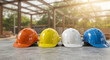 © abu - Four Construction Helmets in Orange Yellow White and Blue on a Wood Table with Blurred Background