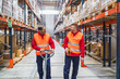© Koldo_Studio - Two warehouse workers are walking and talking in a large logistic center, one is pushing a pallet jack